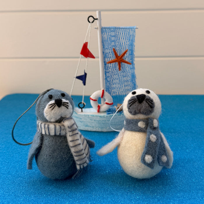 Christmas seals decorations with scarves beside a decorative sailboat on a blue background.
