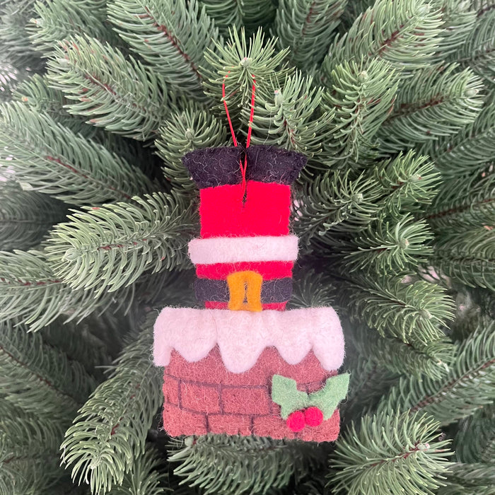 Santa stuck in chimney Christmas decoration hanging on a pine tree branch, featuring felt Santa and chimney design.