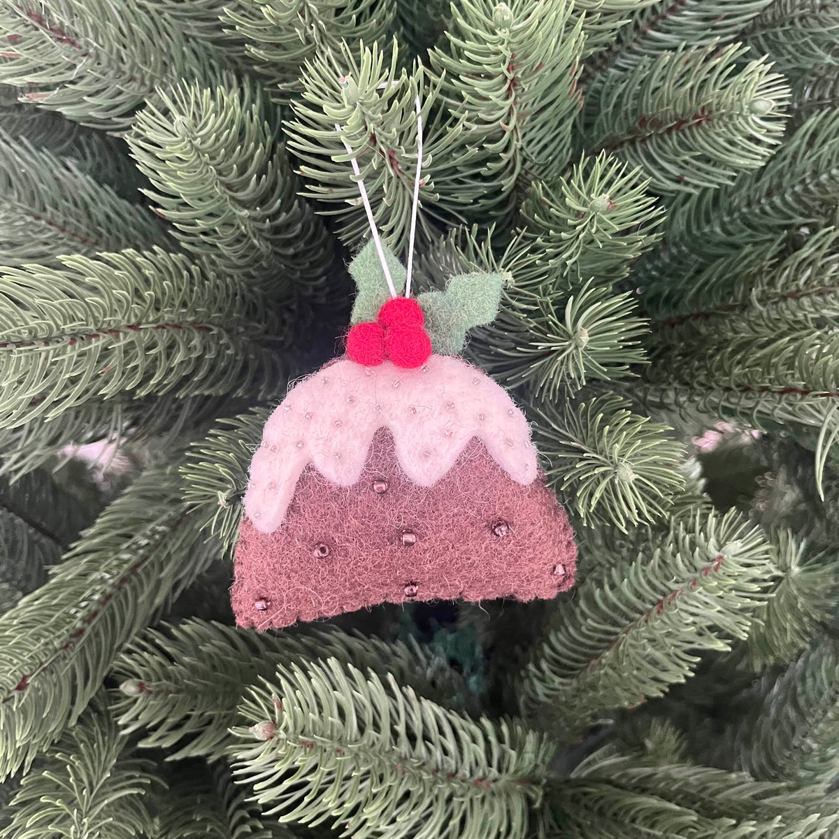 Christmas Pudding Decoration hanging on a pine tree, featuring felt design with berries and icing detail.