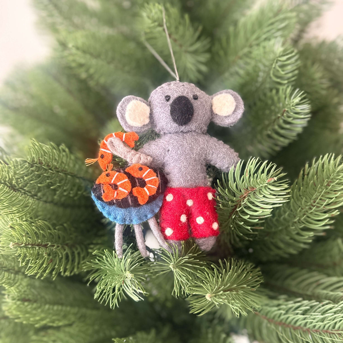 koala with aussie christmas treats decorations wearing red shorts, holding a barbecue with prawns in a Christmas tree.