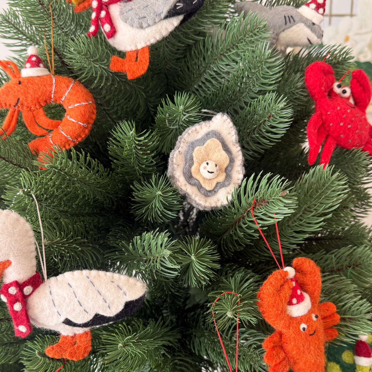 Oyster Christmas decoration hanging on a festive tree, surrounded by colorful felt sea creature ornaments.