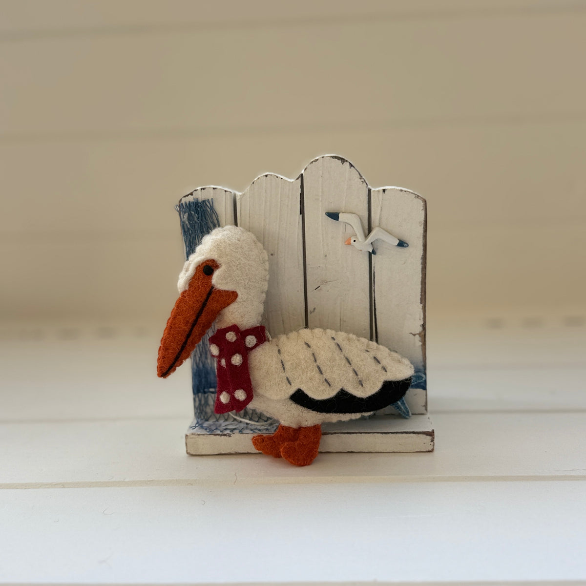Christmas Pelican Decoration perched beside a coastal fence, handmade felt coastal holiday decor.