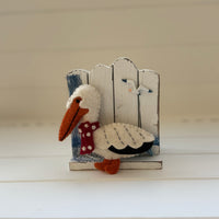 Christmas Pelican Decoration perched beside a coastal fence, handmade felt coastal holiday decor.